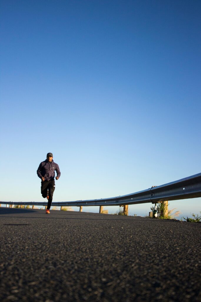 An athletic man jogging on an open road with a clear blue sky in Cape Town, South Africa.